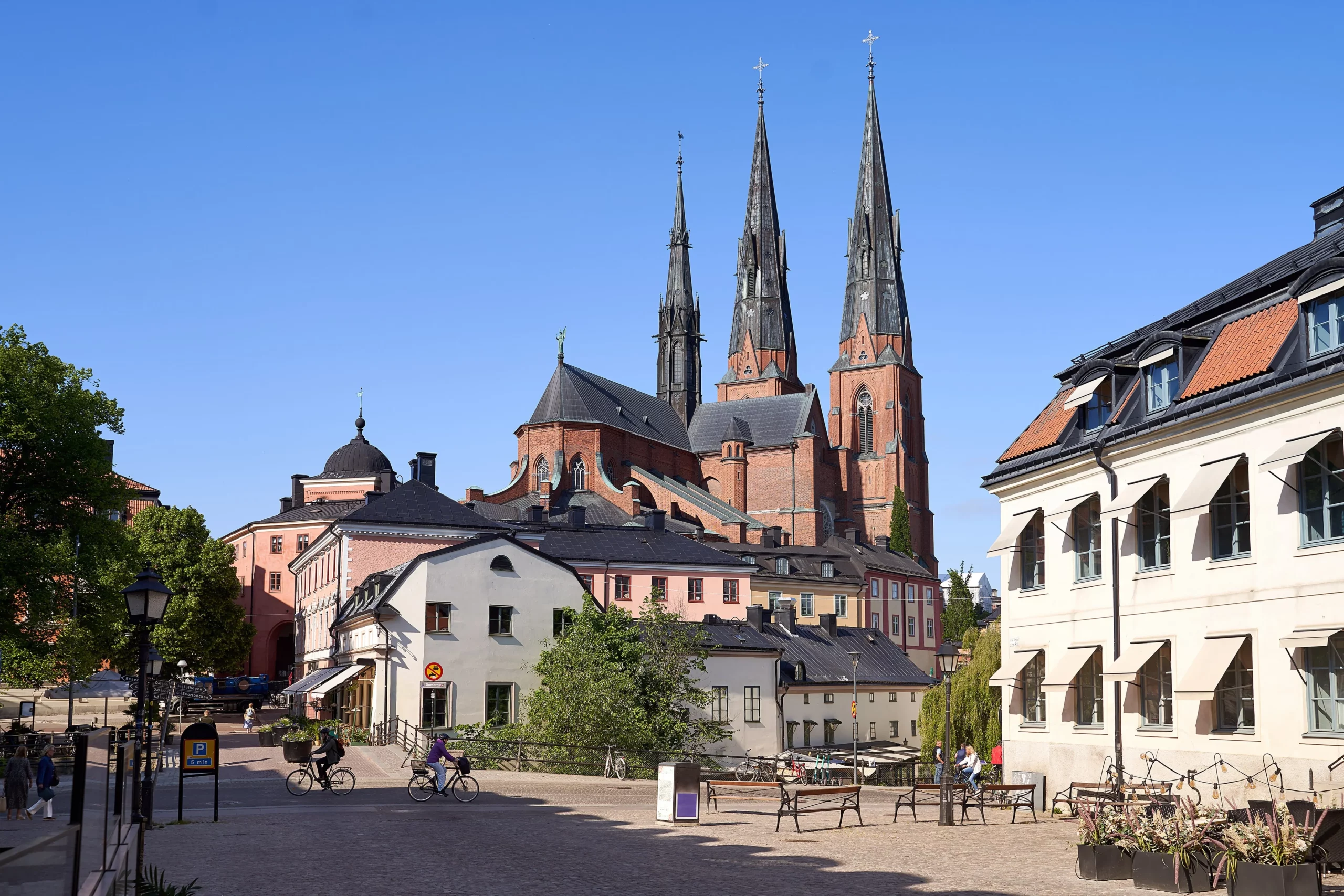 Historisk stadskärna i Uppsala med cyklister, gågata och färgglada byggnader i solljus.